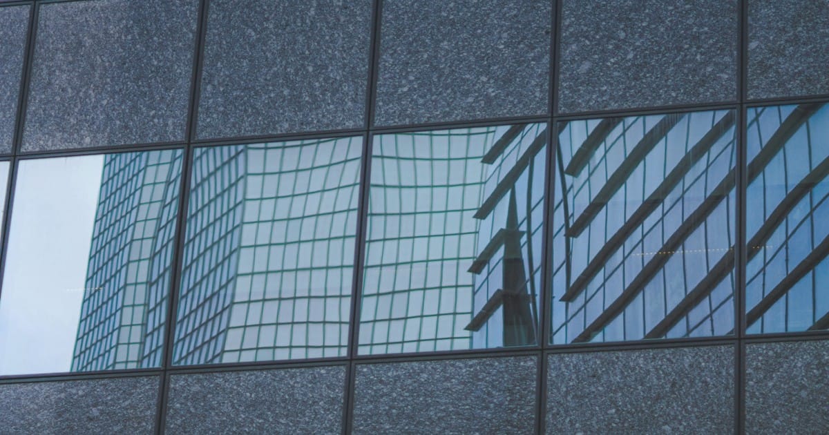 blue glass facade reflecting warped gridlines on a neighboring tower.