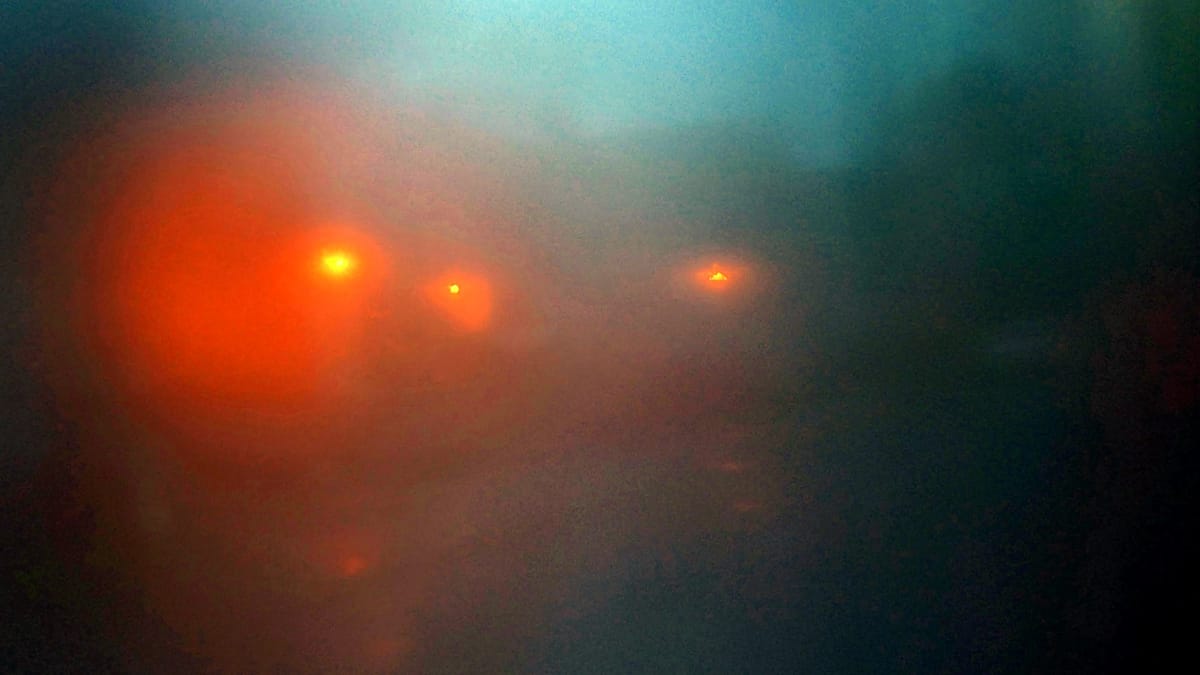 Soft, abstract streetlights glow through heavy fog - warm amber orbs floating in a deep blue haze.