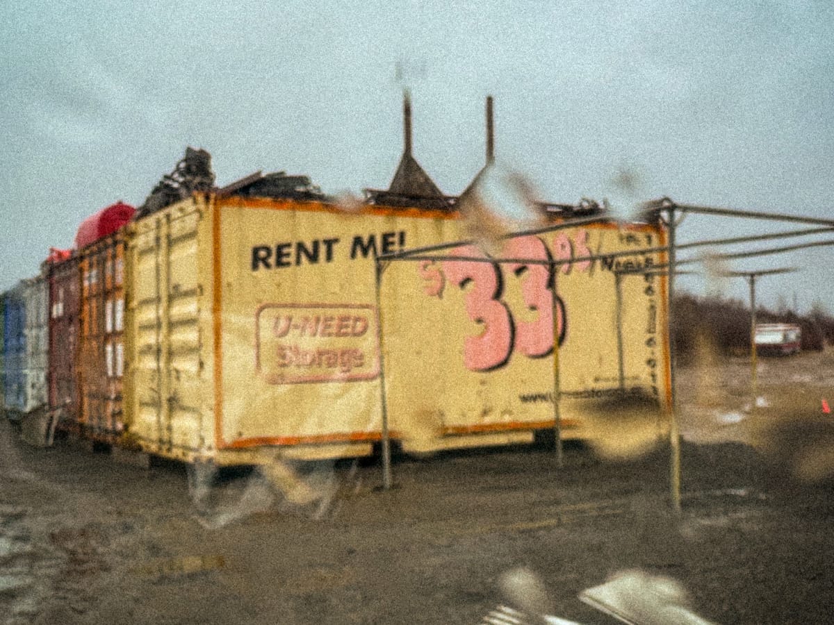 yellow shipping container with ‘rent me’ and pink ‘33 95’ on a rainy day, shot through a windshield.